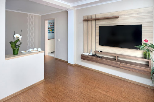 Modern apartment living room with large TV over wooden cabinet Orchid, cork floorboards and door to corridor. 