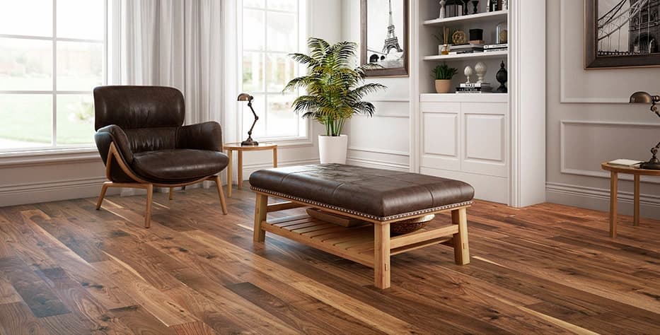 A living room with white walls and two larger windows. There are a matching arm chair and ottoman in leather with wooden legs on a medium-toned laminate floor. 