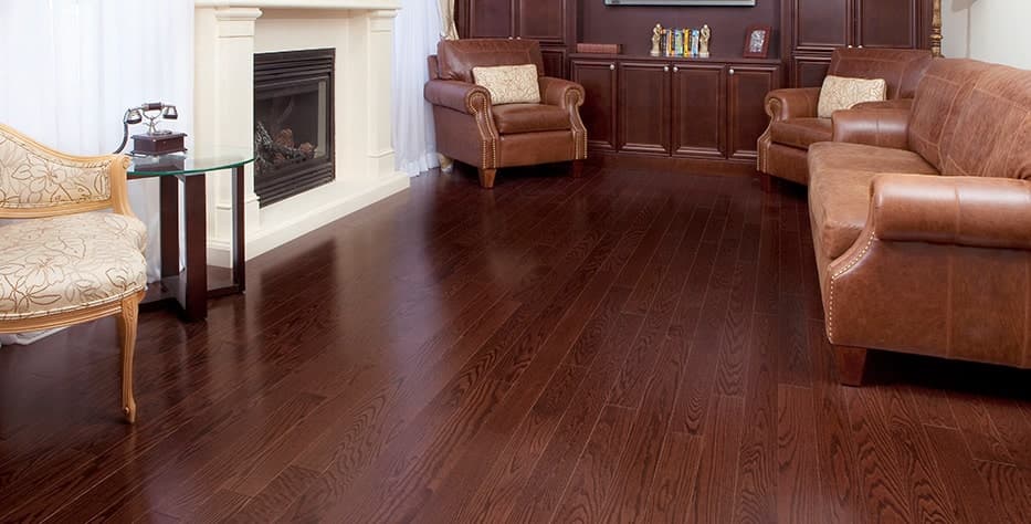 A living room with a white wall with a fireplace and a large built-in dark wood bookshelf on the other wall. The couch and two armchairs are dark brown leather and there is a Queen Anne light coloured arm chair next to an antique phone. The floor is a dark laminate. 